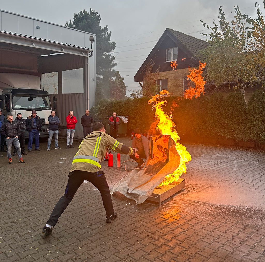 Szkolenie przeciwpożarowe. Mężczyzna próbuje ugasić ogień, rzucając płachtę na wysoki płomień ognia.