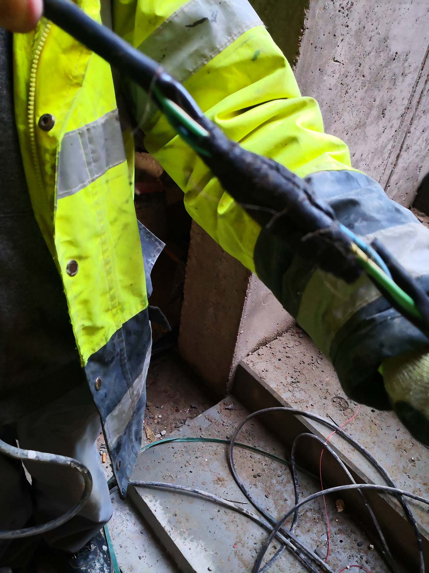 Jak nie powinno wyglądać BHP na budowie. Pracownik pokazuje uszkodzony kabel. Taśma izolacyjna na kablu jest uszkodzona.